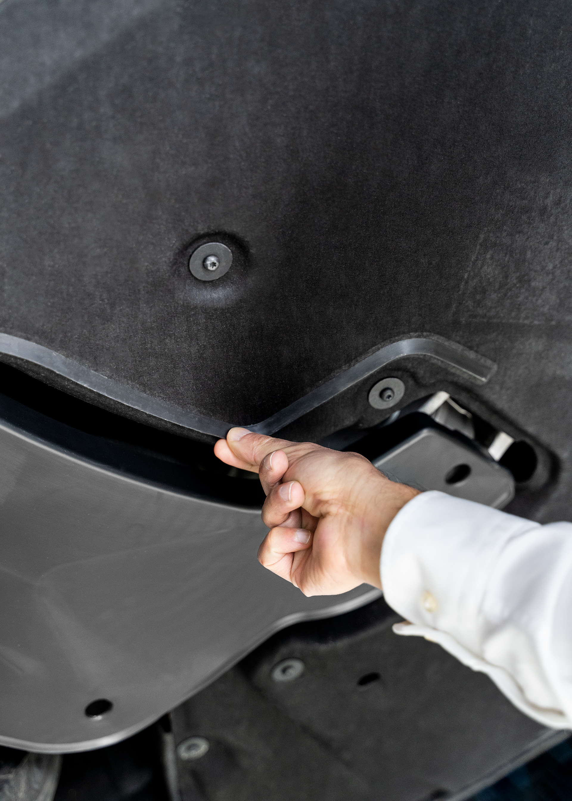 A hand indicates a plastic lip on the vehicle underbody. 